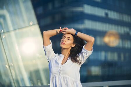 Young business woman over modern glass structure of office building enjoying with closed eyes