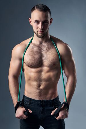 Muscular shirtless man standing with expander over shoulders, looking at camera with intense look