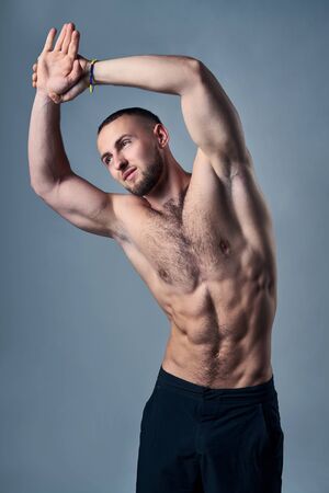 Muscular shirtless man stretching with raised handsの写真素材