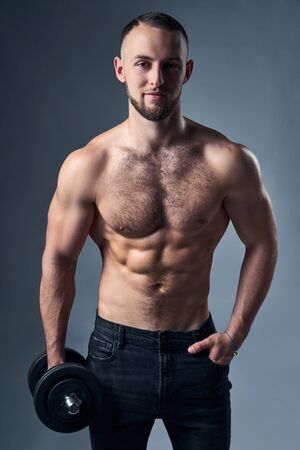 Strong handsome shirtless sport man standing holdina a dumbbell, looking at cameraの写真素材