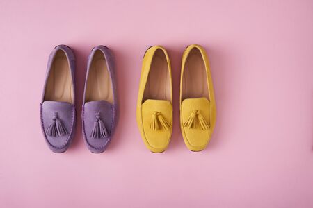 Two pairs of suede moccasins shoes lilac and yellow over pastel pink background, top viewの写真素材