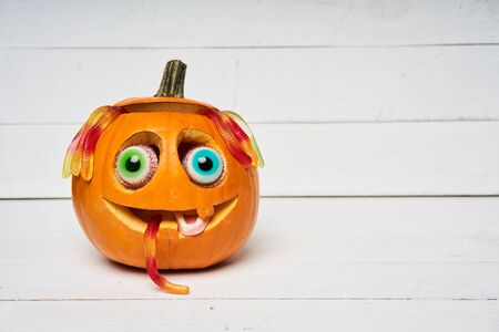 Kind smiling Halloween Pumpkin with candy eyes, teeth and hair of gelatin worms over white wooden planksの写真素材