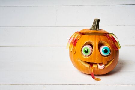 Kind smiling Halloween Pumpkin with candy eyes, teeth and hair of gelatin worms over white wooden planksの写真素材