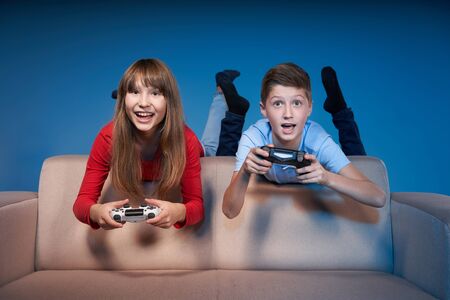 Computer game competition. Gaming concept. Excited children leaning on the sofa back playing video...