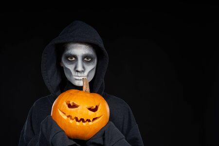 Boy with Halloween makeup holding Jack OLantern pumpkin looking at camera on black backgroundの写真素材