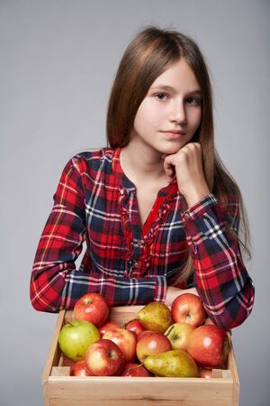 Children, healthy eating and food concept. Portrait a teen girl with apples and pears in a box, studio shot over grey backgroundの写真素材