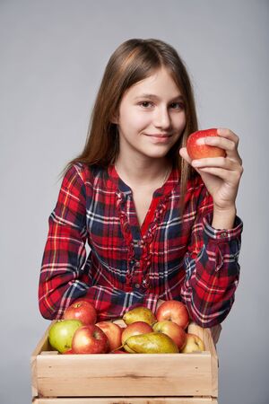 Children, healthy eating and food concept. Portrait a teen girl with apples and pears in a box, studio shot over grey backgroundの写真素材