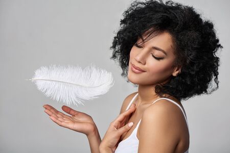 Closeup portrait of beautiful mixed race woman holding white ostrich feather on her palm enjoying its softness and beauty, studio shotの写真素材