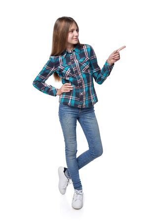 Full length teen girl in checkered shirt standing casually over white background pointing to sideの写真素材
