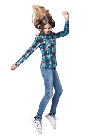 Full length teen girl in checkered shirt dancing listening music in headphones, standing on tiptoe, over white backgroundの写真素材