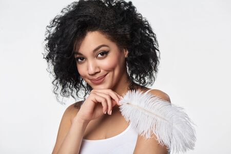 Closeup portrait of beautiful mixed race woman holding white ostrich feather, studio shotの写真素材