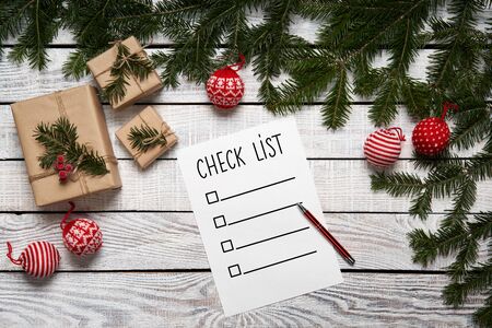 Christmas, New Year check list. Paper sheet with a list on white planks edged by green fir branches with gift boxesの写真素材