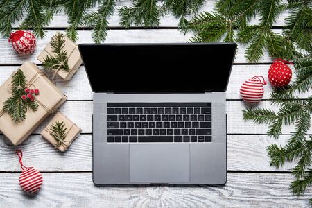 Christmas tree branches and gift boxes on rough white planks with opened laptop with blank screen copy space, top viewの写真素材