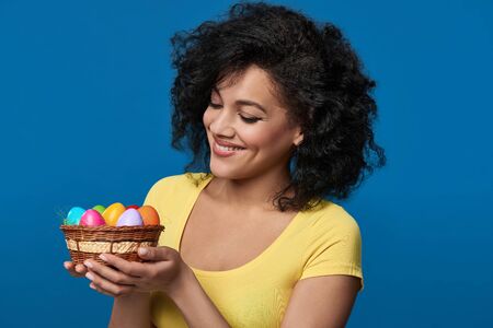 Smiling mixed race woman holding a basket with colorful Easter eggs
