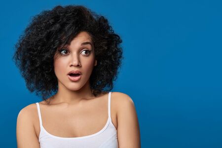 Closeup portrait of surprised mixed race woman looking to side at blank copy space, over blue backgroundの写真素材