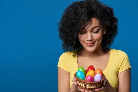 Happy woman holding a basket with colorful Easter eggsの写真素材