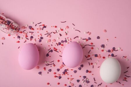 White and pink Easter eggs and bakery decoration scattered on pink backgroundの写真素材