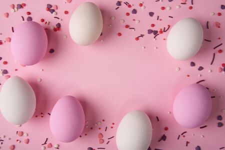 White and pink Easter eggs scattered on pink background with bakery sprinkles, creating a frame with copy spaceの写真素材