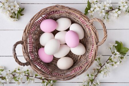 Top view of Easter eggs in willow basket with branch of cherry bloom on white planksの写真素材