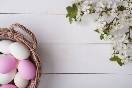 Top view of Easter eggs in willow basket with branch of cherry bloom on white planksの写真素材