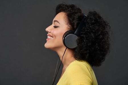 Profile portrait of young mixed race african woman listening music in headphones with closed eyes,...
