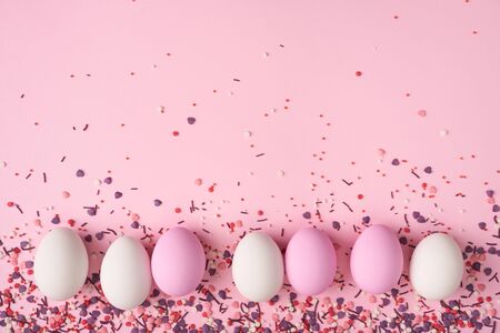 White and pink Easter eggs in line on pink background with bakery sprinkles, creating a copy space aboveの写真素材
