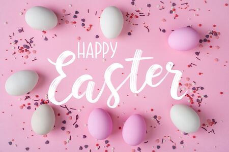 White and pink Easter eggs scattered on pink background with bakery sprinkles, creating a frame with Happy Easter letterting in centerの写真素材
