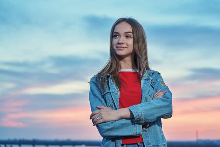 Casual teen girl standing looking away at sunset backgroundの写真素材