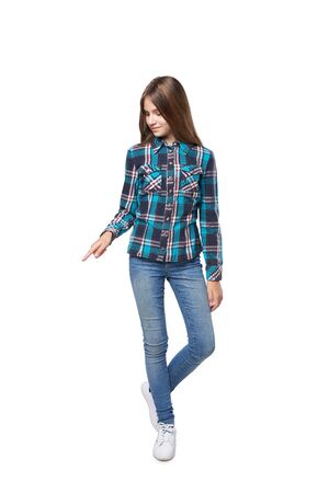 Full length teen girl in checkered shirt standing casually over white background pointing downの写真素材