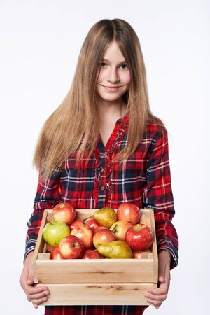 Children, healthy eating and food concept. Portrait of teen girl holding a wooden box full of apples and pears, studio shot over white backgroundの写真素材