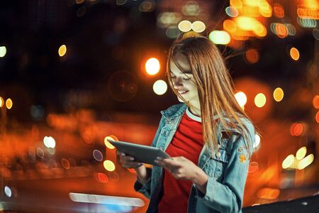 Lovely teen girl on night cityscape background with street lights, using a digital tabletの写真素材
