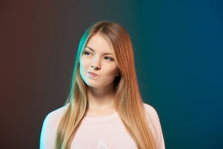 Young smiling female with colorful backlight looking away contemplating with squeezed lips, closeup studio portraitの写真素材