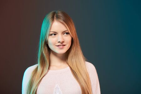Young smiling female with colorful backlight looking to side at blank copy space, closeup studio portraitの写真素材