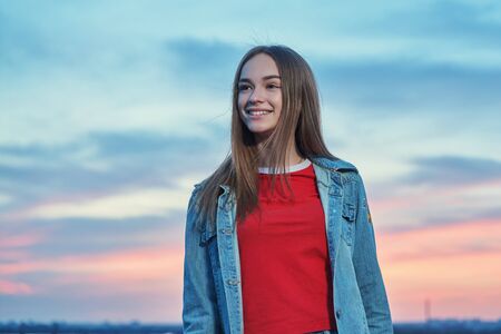 Casual teen girl standing looking away at sunset backgroundの写真素材