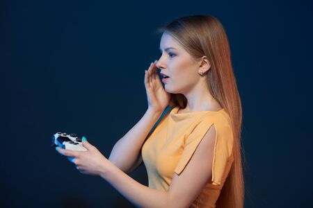 Gamer girl. Profile of surprised girl playing video game with joystick on blue backgroundの写真素材