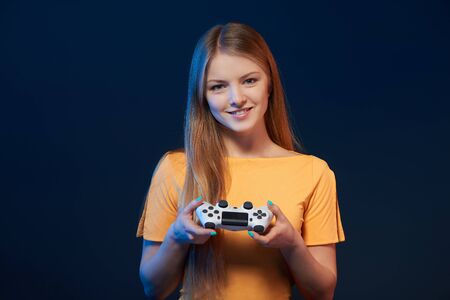 Gamer girl. Smiling girl holding video game joystick on blue backgroundの写真素材