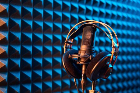 Studio condenser microphone with professional headphones on blue acoustic foam panel backgroundの写真素材