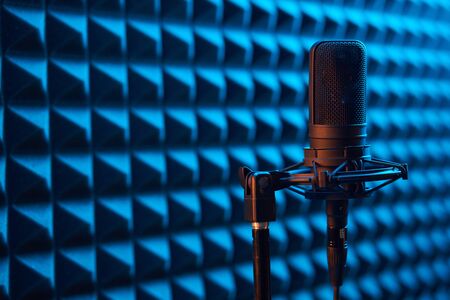 Studio condenser microphone on blue acoustic foam panel background with copy space on leftの写真素材