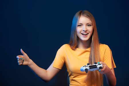 Gamer girl. Happy girl holding video game joystick giving thum up, on blue backgroundの写真素材