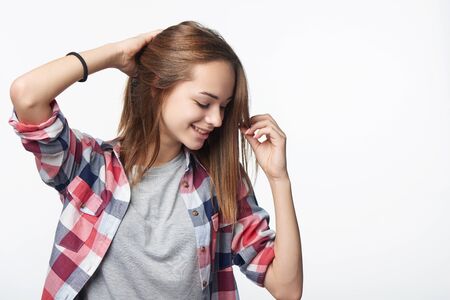 Smiling relaxed teen girl touching her hair looking down, studio portraitの写真素材