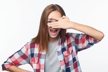 Emotional joyful teen girl peeking through fingers, studio portraitの写真素材