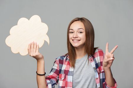 Happy teen girl holding thinking bubble and gesturing V sign, studio portrait