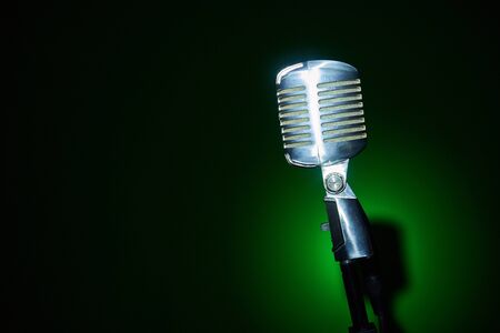 Studio retro condenser microphone on green spot light background, copy space on leftの写真素材