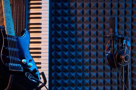 Electric guitar, piano and microphone with professional headphones over acoustic foam panel background, with copy spaceの写真素材