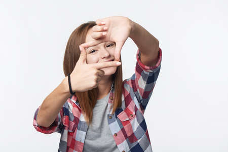 Smiling teen girl looking at camera through finger frame, studio portraitの写真素材