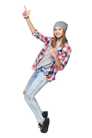 Smiling teen girl standing in full length on tiptoe pointing to side at blank copy space, isolated on whiteの写真素材