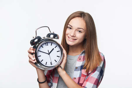 Smiling teen girl holding big clock, isolated portrait over white background. Time conceptの写真素材