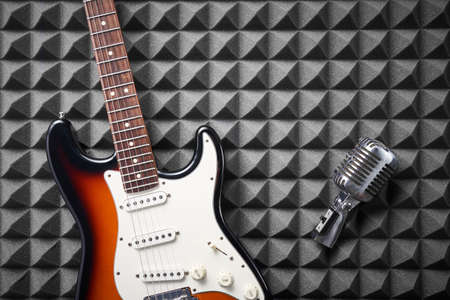 Electric guitar and retro microphone on acoustic foam panel backgroundの写真素材