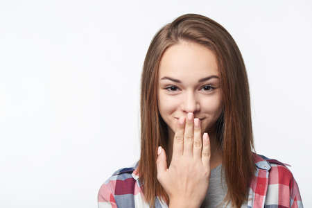 Closeup of shy smiling teen girl covering her mouth by palm, looking at cameraの写真素材