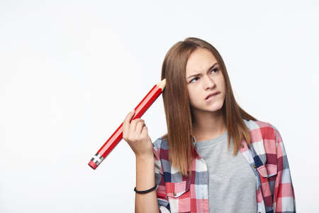 Unsure contemplating girl scratching her head with big pencil frowning her eyebrows looking away to the blank copy spaceの写真素材
